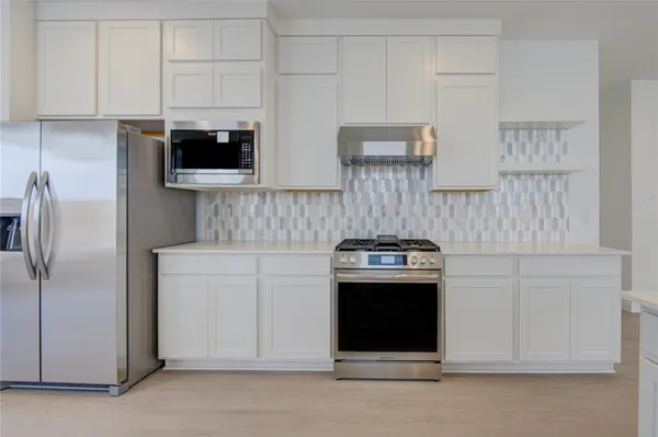 a kitchen with stainless steel appliances granite countertop white cabinets a refrigerator a sink a stove and white cabinets