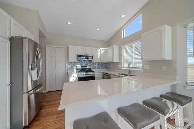 a kitchen with granite countertop a refrigerator a sink dishwasher a stove top oven a refrigerator and white cabinets with wooden floor