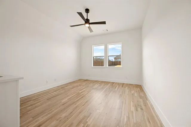 an empty room with wooden floor ceiling fan and windows