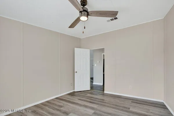 an empty room with wooden floor chandelier fan and windows