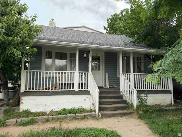 Charming bungalow featuring light blue siding, a dark gray shingle roof, and a white-railed covered porch