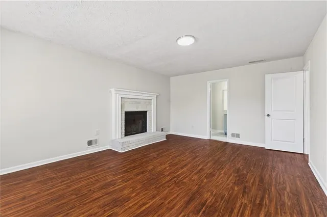 a view of an empty room with wooden floor and a fireplace