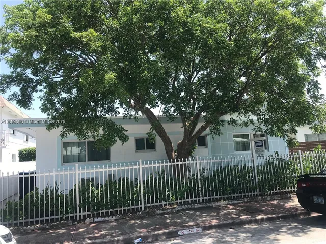 a view of a white house with a large tree and wooden fence