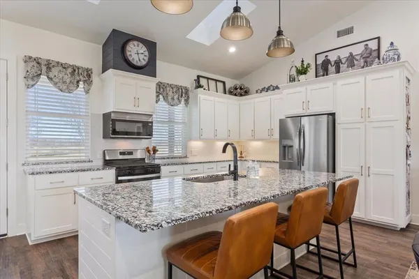 a kitchen with stainless steel appliances granite countertop a stove a refrigerator a microwave a sink and white cabinets with wooden floors