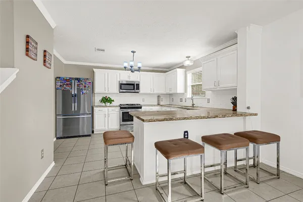 a kitchen with stainless steel appliances granite countertop a sink a stove a refrigerator cabinets and chairs