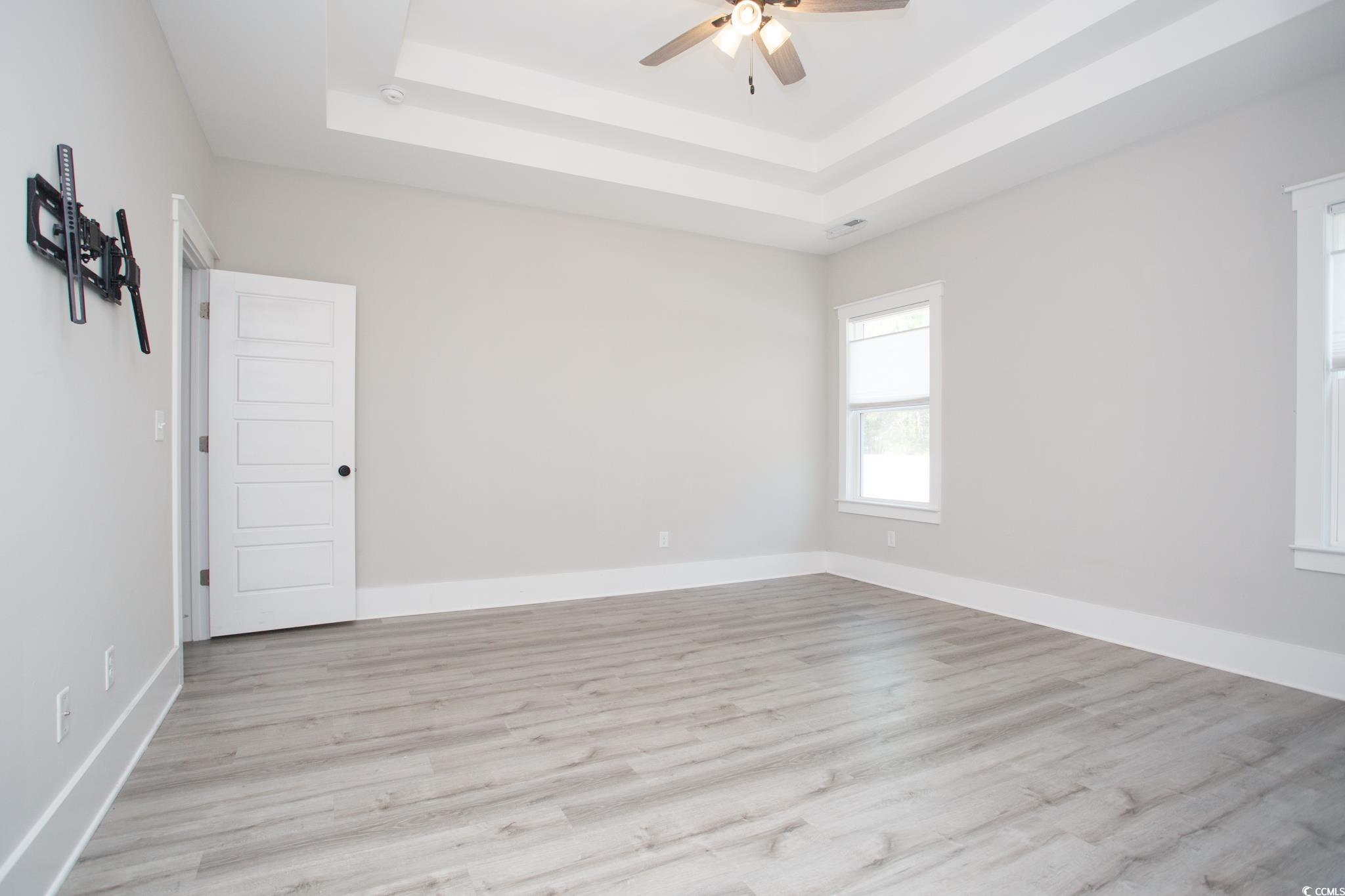 261 Marsh Tacky Loop Myrtle Beach, SC 29588 - Photo 19 of 40 Empty room with ceiling fan, a raised ceiling, and light hardwood / wood-style flooring