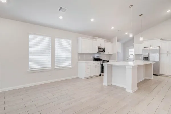 a large white kitchen with kitchen island a stove a sink a refrigerator and white cabinets with wooden floor