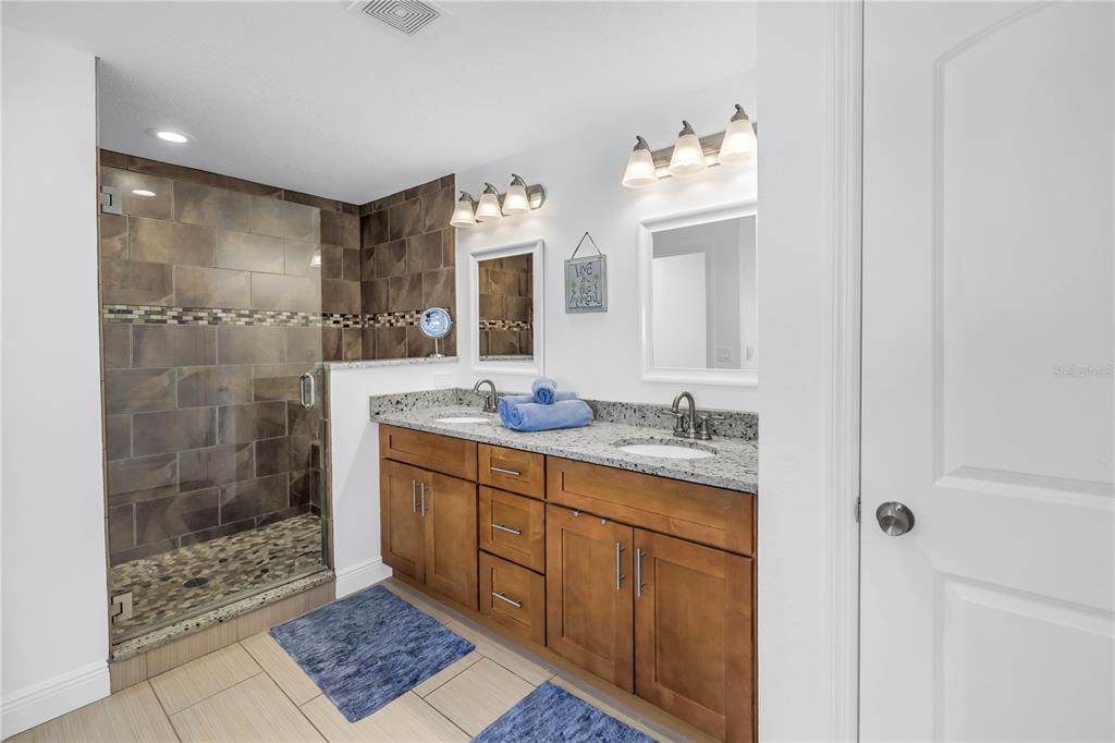 100 Windrush Boulevard, Unit 1 Indian Rocks Beach, FL 33785 - Photo 17 of 37 a bathroom with a granite countertop sink a mirror and a shower