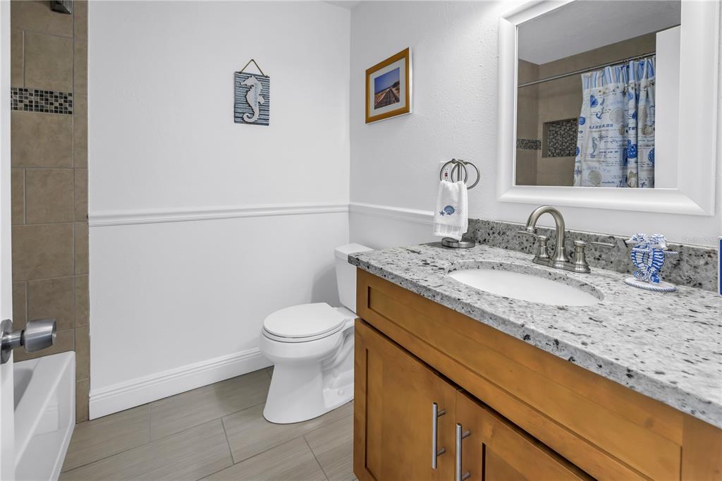 100 Windrush Boulevard, Unit 1 Indian Rocks Beach, FL 33785 - Photo 21 of 37 a bathroom with a granite countertop sink a toilet and a mirror