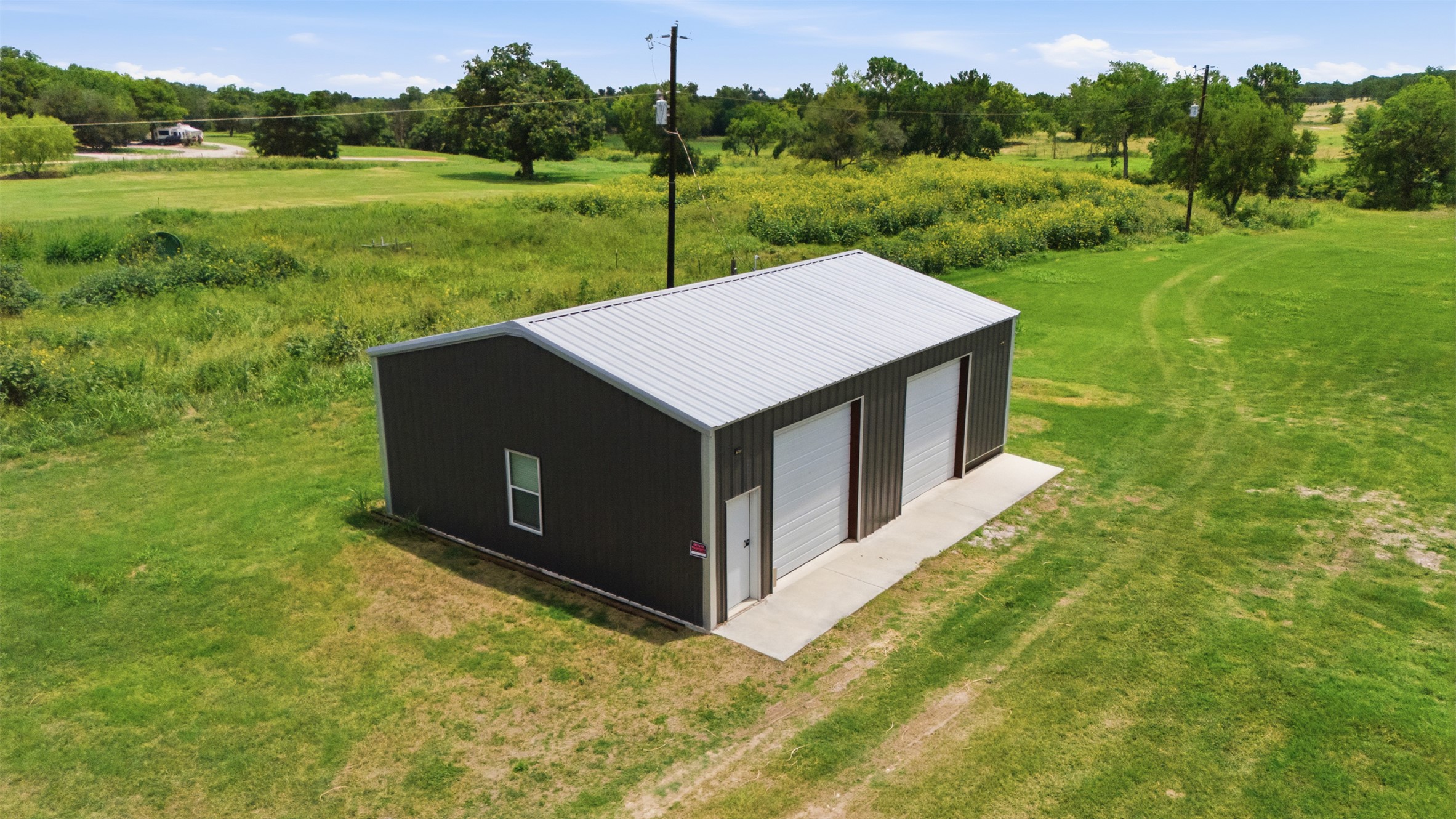 2043 Fm 971 Georgetown, TX 78626 - Photo 4 of 12 A versatile metal structure with multiple bay doors, set against a backdrop of open green space.