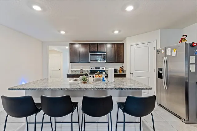 a kitchen with stainless steel appliances granite countertop a dining table chairs refrigerator and cabinets