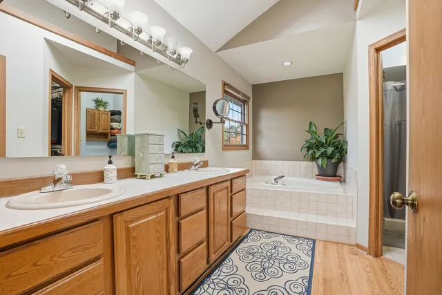 a spacious bathroom with a double vanity sink a large mirror a bathtub and next to a window