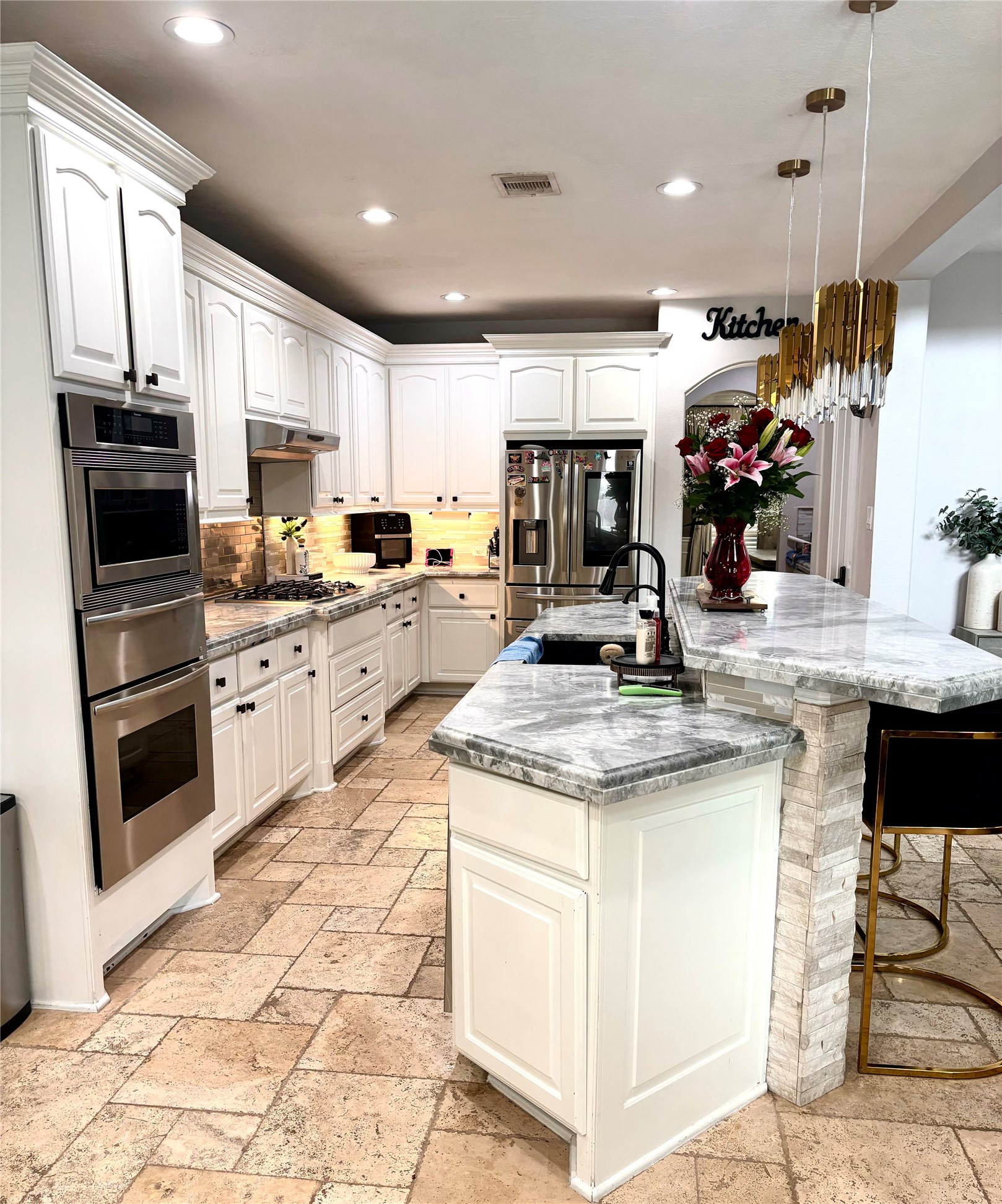13510 Cascade Caverns Court Houston, TX 77044 - Photo 25 of 37 A modern and bright kitchen featuring white cabinetry, high-end appliances, a central island with seating, and elegant lighting fixtures. The space has stone countertops and a tiled floor, combining functionality with a luxurious feel.