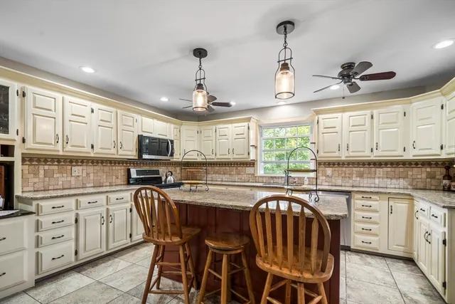 a kitchen with stainless steel appliances granite countertop a stove a sink a microwave oven a refrigerator with white cabinets and wooden floor