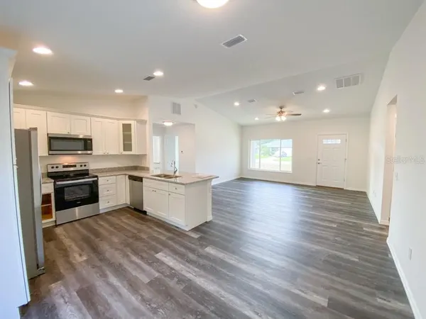 a large kitchen with kitchen island a sink dishwasher stove and white cabinets with wooden floor