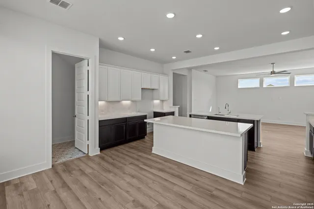 a large white kitchen with kitchen island a sink wooden floor and a refrigerator