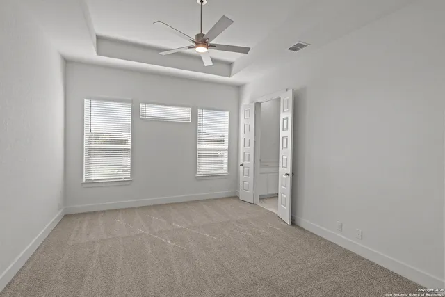 an empty room with chandelier fan and windows