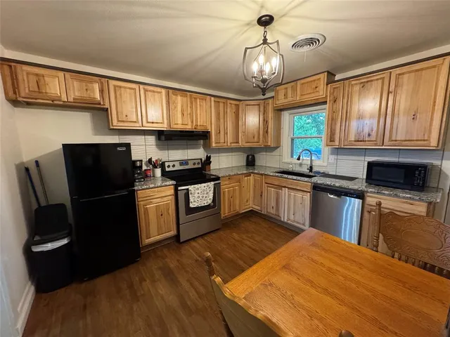 a kitchen with granite countertop a refrigerator a sink dishwasher a stove and white cabinets with wooden floor