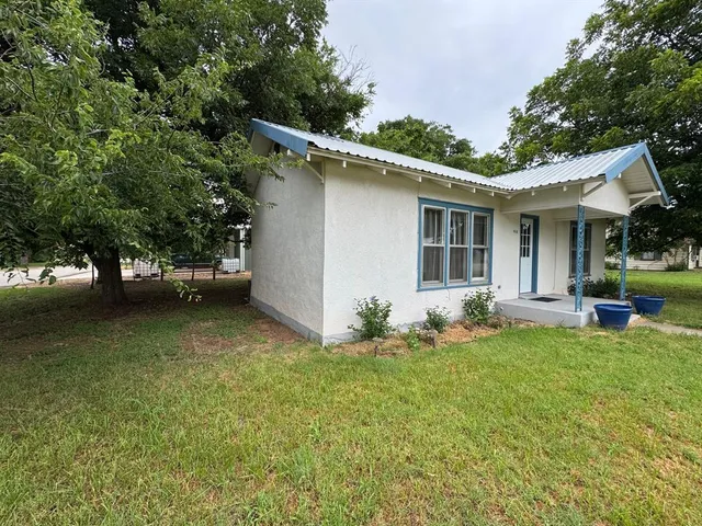 a backyard of a house with table and chairs plants and large tree