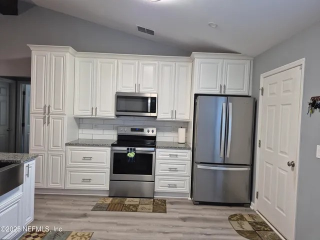 a kitchen with stainless steel appliances granite countertop a refrigerator stove and white cabinets