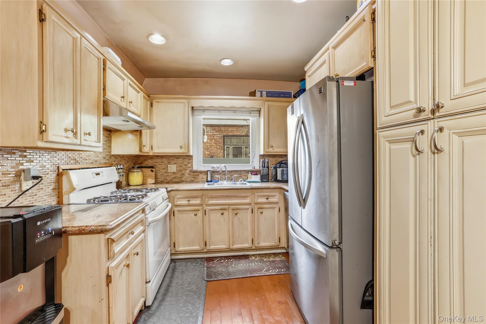 83-39 252nd Street Queens, NY 11426 - Photo 9 of 26 Kitchen featuring light wood cabinetry, a mosaic tile backsplash, a stainless steel refrigerator, and built-in overhead lighting