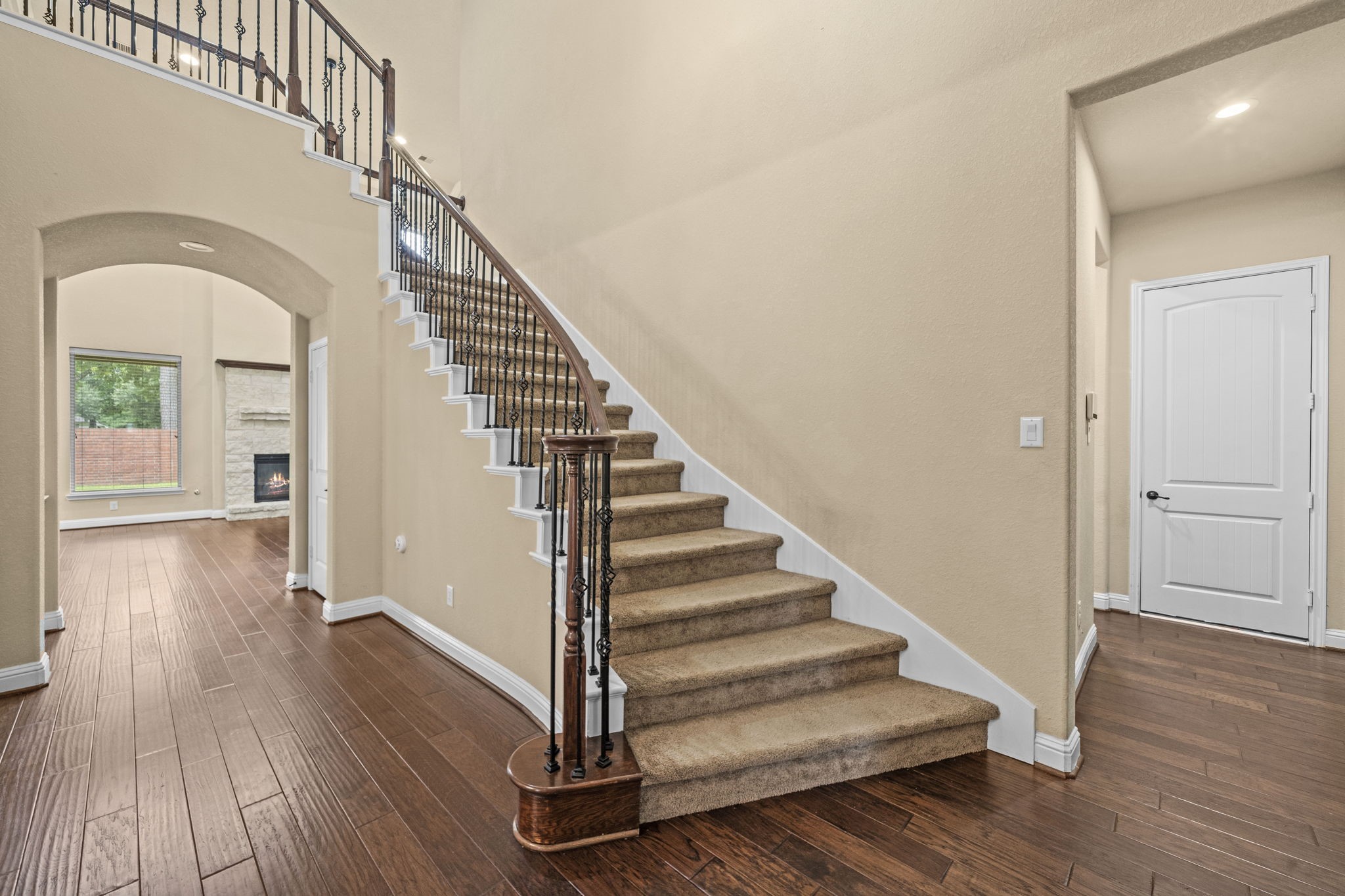 14215 Spindle Arbor Road Cypress, TX 77429 - Photo 10 of 47 This photo showcases an inviting entryway with a carpeted staircase and elegant wrought iron railing. The space features hardwood floors and leads to a bright living area with large windows and a fireplace.