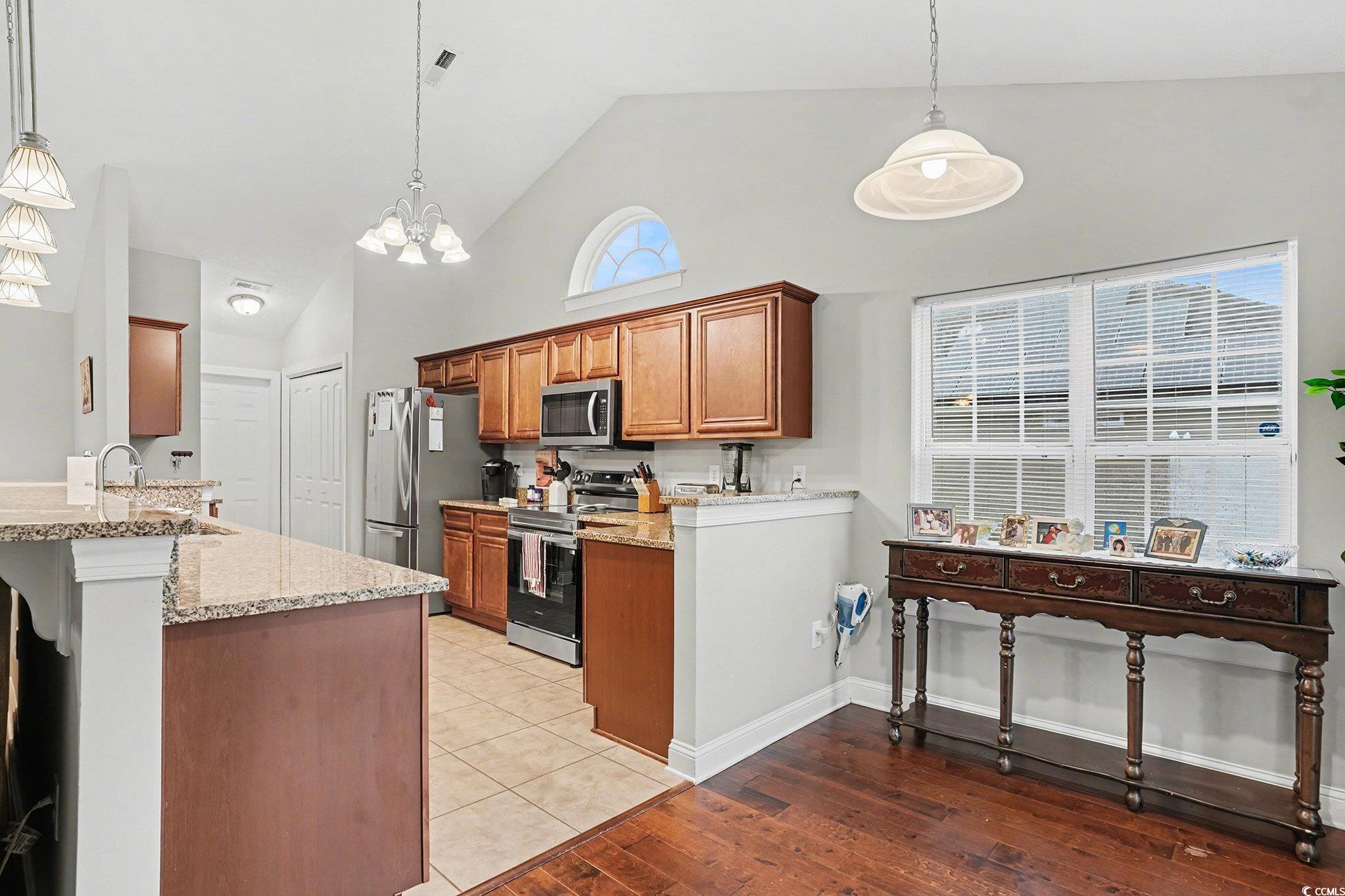 216 Camrose Way Myrtle Beach, SC 29588 - Photo 8 of 32 Kitchen with brown cabinets, hanging light fixtures, appliances with stainless steel finishes, light stone counters, and high vaulted ceiling