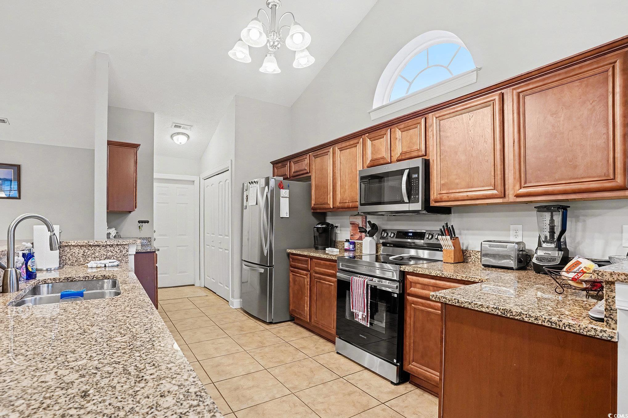 216 Camrose Way Myrtle Beach, SC 29588 - Photo 10 of 32 Kitchen featuring high vaulted ceiling, light stone counters, appliances with stainless steel finishes, brown cabinets, and hanging light fixtures