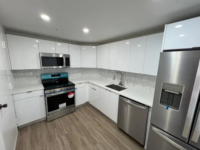 a kitchen with granite countertop a refrigerator a stove top oven a sink and cabinets