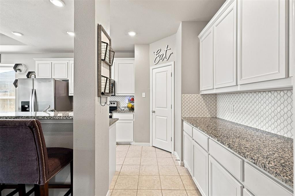 1321 Raleigh Path Denton, TX 76208 - Photo 17 of 35 Kitchen featuring white cabinetry with crown molding, light-toned granite countertops, and a white patterned tile backsplash