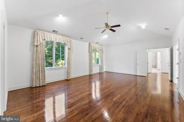 an empty room with wooden floor fan and windows