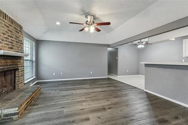 an empty room with wooden floor a chandelier fan and a fireplace