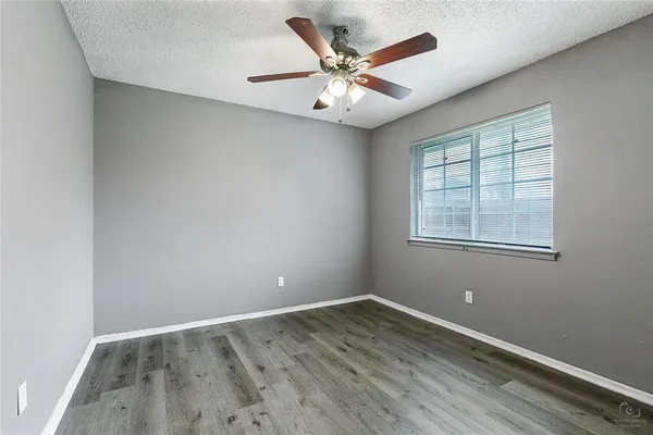 an empty room with wooden floor fan and windows