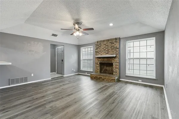 an empty room with wooden floor fireplace and windows