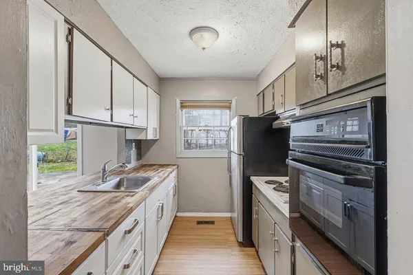 a kitchen with granite countertop a refrigerator a sink dishwasher a stove and white cabinets with wooden floor