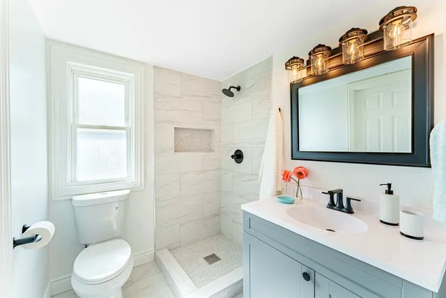 a bathroom with a toilet a sink a mirror a window and vanity