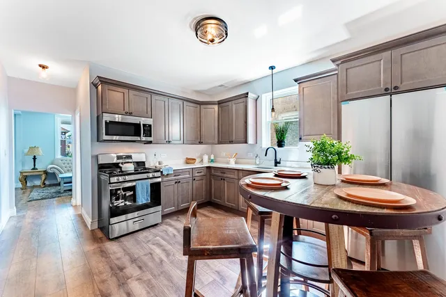 a kitchen with stainless steel appliances granite countertop a stove top oven a refrigerator a sink and a dining table with wooden floor