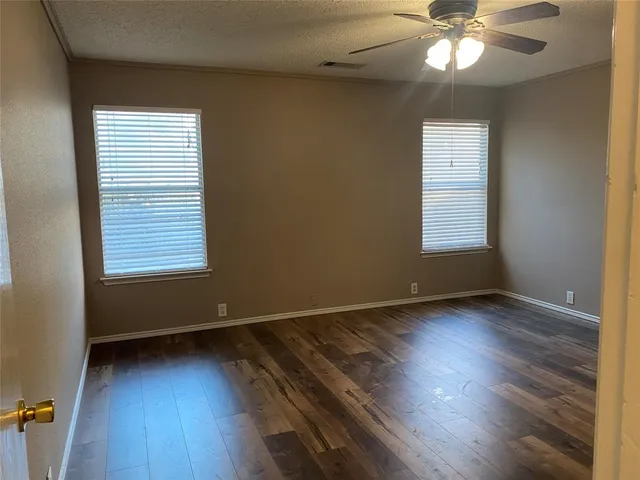an empty room with wooden floor fan and windows