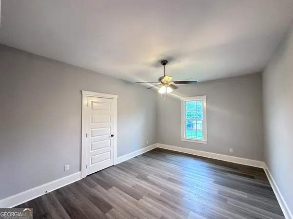 an empty room with wooden floor chandelier fan and windows
