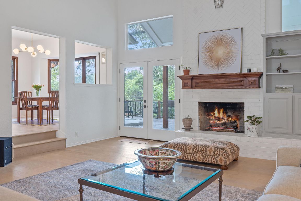 6302 Gato Path Austin, TX 78731 - Photo 2 of 37 Living area with wood finished floors, a brick fireplace, a towering ceiling, a chandelier, and french doors