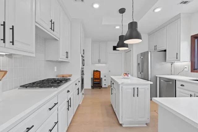 a kitchen that has a lot of white cabinets and stainless steel appliances