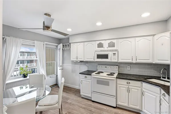 a kitchen with stainless steel appliances white cabinets a stove a sink and a dining table with wooden floor