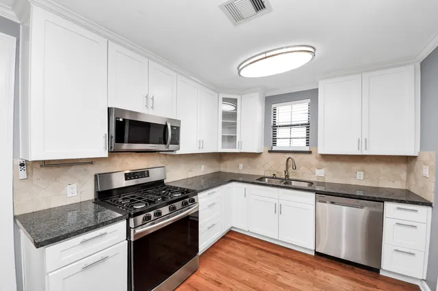 a kitchen with granite countertop a stove top oven a sink dishwasher and white cabinets with wooden floor