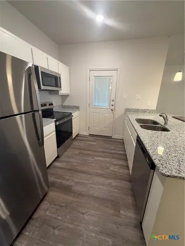 a kitchen with stainless steel appliances granite countertop a refrigerator a stove and a sink with wooden floor