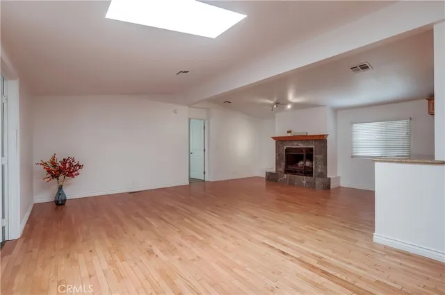a view of an empty room with wooden floor a fireplace and a window