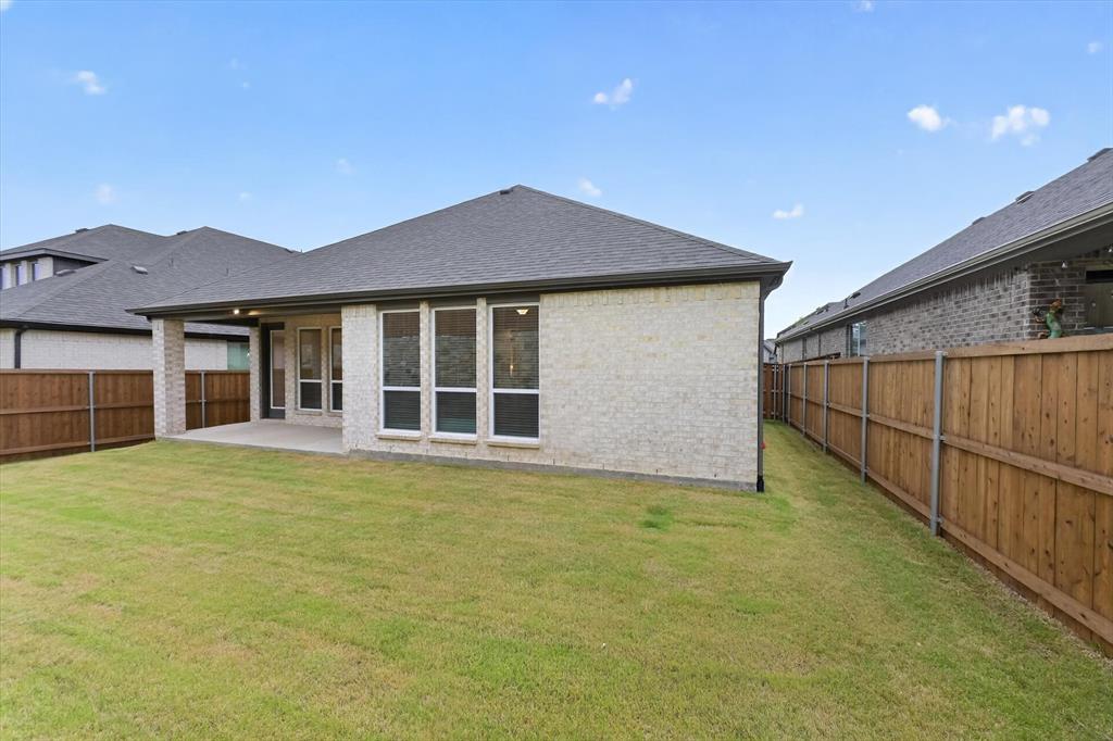 4123 Windy Point Court Oak Point, TX 75068 - Photo 5 of 29 Expansive grass lawn featuring a covered concrete patio, light-colored brick exterior, dark grey shingle roof, and a wood privacy fence