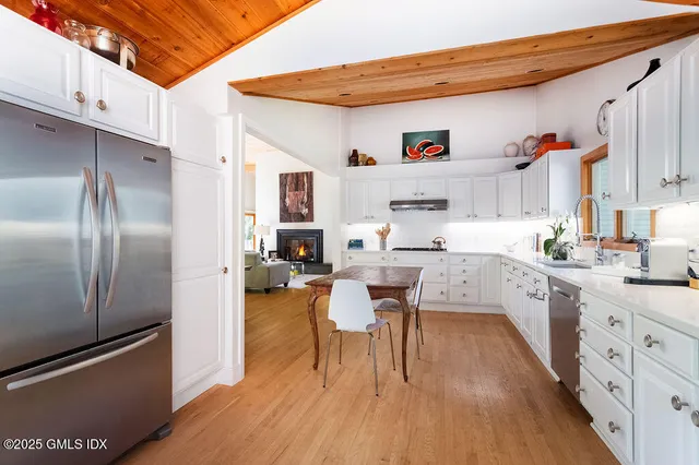 a large white kitchen with a refrigerator a microwave oven a sink dishwasher and white cabinets with wooden floor