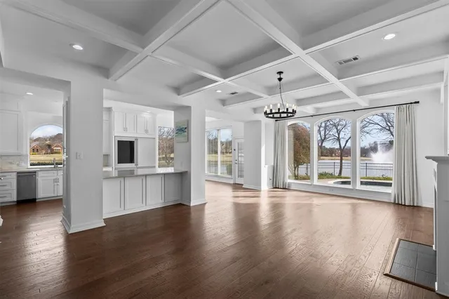 a view of an empty room with wooden floor and a kitchen