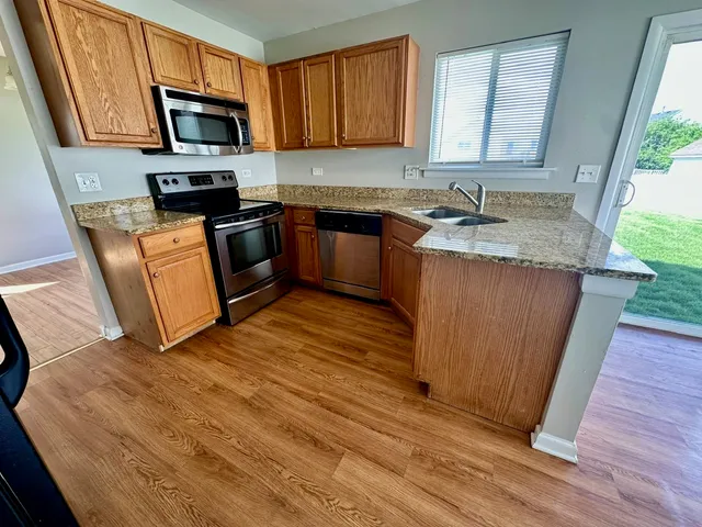 a kitchen with granite countertop a sink a stove top oven a refrigerator cabinets and wooden floor