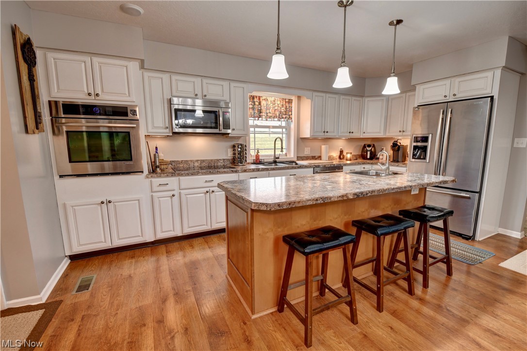 4301 Murray Road Dover, OH 44622 - Photo 7 of 49 Kitchen featuring white cabinets, stainless steel appliances, an island with sink, and light hardwood / wood-style floors